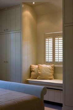 a white bed sitting next to a window with shutters on the windows sill