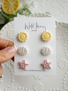 a person holding two small seashells and starfish earrings on top of a white plate