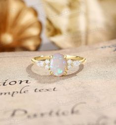 an opal and diamond ring sitting on top of a piece of paper with shells in the background