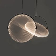 two circular lights hanging from the ceiling in front of a white wall and black background