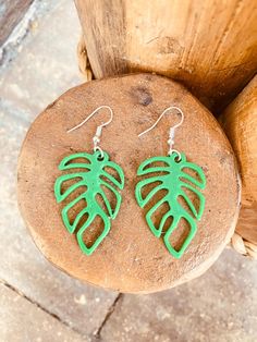 a pair of green leaf earrings sitting on top of a stone slab next to a piece of wood