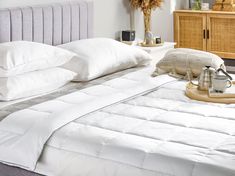 a bed with white sheets and pillows on top of it next to a wooden dresser