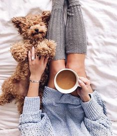 two women and a dog laying on a bed with their legs crossed holding coffee cups