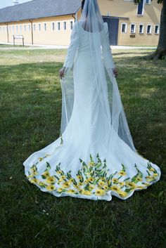 a woman in a white wedding dress with sunflowers on the skirt and veil