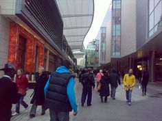 many people are walking down the sidewalk in front of some buildings