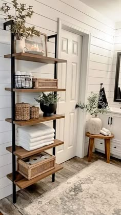 a bathroom with white walls and wooden shelves filled with towels, plants and baskets on top of them