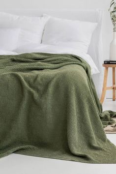 a bed with a green blanket on top of it next to a night stand and lamp