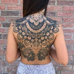 the back of a woman's body with an intricate tattoo on her upper half