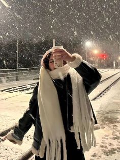 a woman is standing in the snow holding her scarf over her face and covering her eyes