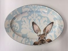 a blue and white plate with a brown rabbit on it's face in front of a damask background