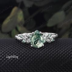 a ring with an oval green stone surrounded by leafy leaves on top of it