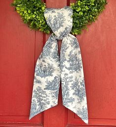 a blue and white bow tie hanging on a red door with a green boxwood wreath