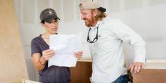 a man and woman standing next to each other while looking at something on a piece of paper