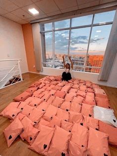 a person laying on top of a bed covered in pink sheets and pillows with windows overlooking the city