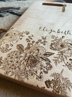 a wooden cutting board with flowers and the words elizabeth on it, sitting on a table