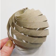 a hand holding a ball made out of brown paper with strips of tape on it