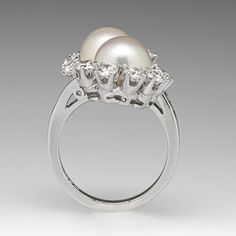 This captivating by-pass style ring is centered with two (2), post set, cultured saltwater pearls. The pearls are each bordered with six (6), prong set, round brilliant cut diamonds. The top face of the shank is accented with six (6), channel set, baguette cut diamonds on each side. The ring measures 24.1mm at the top, rises 10.0mm above the finger, tapering to 1.9mm wide and 1.6mm thick at the base of the shank. This ring is currently a size 6. The pearls in this ring appear to be from a strand Akoya Pearl Ring With Diamond Accents For Anniversary, Anniversary Akoya Pearl Ring With Diamond Accents, Formal Multi-stone Pearl Ring In Fine Jewelry Style, Formal White Multi-stone Pearl Ring, Classic Multi-stone Pearl Ring For Formal Occasions, Akoya Pearl Ring With Brilliant Cut For Anniversary, Elegant Formal Multi-stone Pearl Ring, Multi-stone Diamond Pearl Ring For Wedding, Vintage Twins