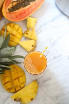 a pineapple and orange drink on a marble table with slices of fruit around it