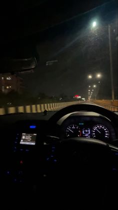 the dashboard of a car at night with street lights in the back ground and cars driving by