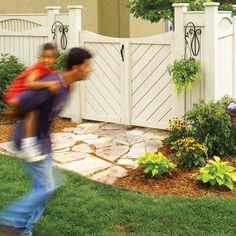 a man carrying a child in his arms near a fence and flowerbedding area