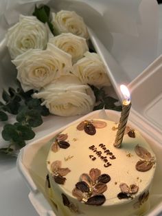 a birthday cake with a lit candle on it next to white roses and greenery