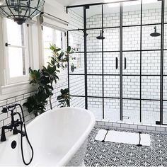 a white bath tub sitting next to a window in a bathroom with black and white tile