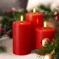 three red candles sitting on top of a table next to christmas decorations and greenery