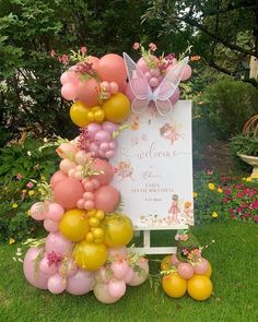 a sign with balloons attached to it in front of some flowers and plants on the grass