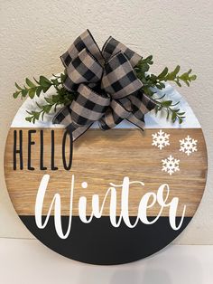 a wooden sign that says hello winter with snowflakes on it and a bow