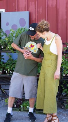 a man and woman standing next to each other in front of some potted plants