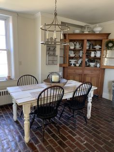 a dining room table with chairs and a china cabinet in the back ground, next to a brick floor