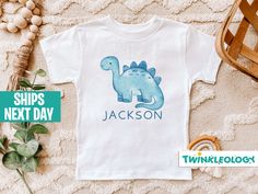 "Personalized Dinosaur Kids Shirt - Cute Dinosaur Name Toddler Shirt - Personalized Custom Name Toddler Shirt If you're like us and love your kid looking cute all the time, then this super soft, Custom Dinosaur Shirt is going to make your day! Designed with stylish mamas in mind. **Sizing Tip** Shirts are designed on 100% Cotton. They tend to run true to size. They have a ribbed collar, double needle stitched and bottom hemmed. HOW TO ORDER: 1. Choose the quantity you would like to purchase. 2. Enter any specific notes you would like seller to know in the \"Note to Seller\" section. 3. Click \"Add to cart\". For multiple items go back to the listings and repeat the same steps /DETAILS - 100% Cotton - Machine Washable - Short Sleeve - 100% Handmade in the USA /CARE INSTRUCTIONS - Turn Garme Blue Dinosaur Print Long Sleeve Top, Blue Long Sleeve Dinosaur Print Top, Long Sleeve Blue Top With Dinosaur Print, Blue Long Sleeve Top With Dinosaur Print, Fitted Short Sleeve Dinosaur Print Top, Fitted Short Sleeve Tops With Dinosaur Print, Fitted Cotton Tops With Dinosaur Print, Casual Fitted Dinosaur Print Top, Fitted Casual Top With Dinosaur Print