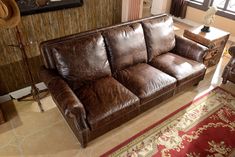 a brown leather couch sitting in a living room next to a red and white rug