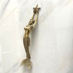 a gold mermaid figurine holding a star on it's back, against a white marble background