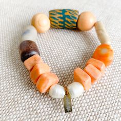 Sustainable Bracelet. A bright bold green hand painted prayer bead with neutral rosewood and soft peach beads. African prayer beads from Africa’s Ivory Coast for loyalty, love and health. Featuires orange coral stone. Rosewood from the tree of health and wisdom. Freshwater large pearls in mint. Sterling silver BelleStyle logo tag. Comes in linen travel pouch. One of a kind. Made in USA. Artisan Wooden Beads Bracelet For Meditation, Earthy Wooden Beaded Bracelets As Gift, Earthy Wooden Beaded Bracelets For Gift, Spiritual Wooden Beads Stretch Bracelet For Healing, Handmade Orange Beaded Bracelets For Meditation, Artisan Wooden Beads Bracelets For Meditation, Unique Wooden Beads Bracelet For Healing, Handmade Spiritual Orange Stretch Bracelet, Unique Wooden Beaded Bracelets For Healing