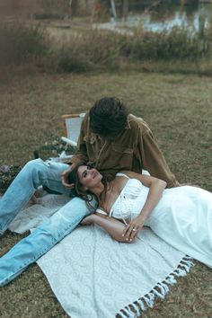 a woman laying on top of a blanket next to a man sitting on the ground