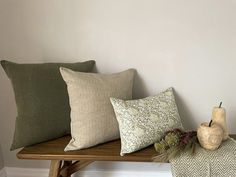 four pillows on a wooden bench in front of a white wall and vase with flowers