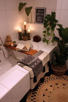 a bath room with a tub and a book on the counter next to candles, potted plants and a rug