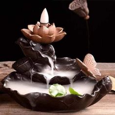 a decorative fountain with flowers and butterflies in it on a wooden table next to a plant