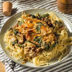 a white plate topped with pasta and meat covered in sauce on top of a striped table cloth