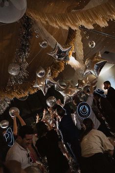 a group of people standing around each other in a room with lights and decorations hanging from the ceiling