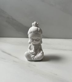 a small white buddha figurine sitting on a table with a marble slab in the background