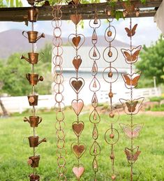 several metal hearts hanging from the side of a fence in front of a barn with grass and trees