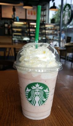 a starbucks drink with whipped cream and a green straw in a cup on a table