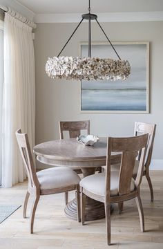 a chandelier hangs over a dining room table with chairs and a painting on the wall