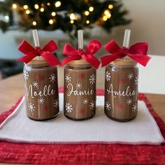 three brown jars with red bows are sitting on a white towel near a christmas tree