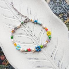 a bracelet with multicolored beads and charms on a white plate next to a leaf