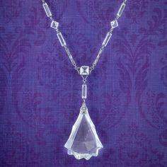 A fabulous Art Deco lavaliere necklace from the early 20th Century adorned with a large glass pendant hanging from the bottom. The glass has been expertly cut into a striking teardrop shape with glistening facets and a jagged edge.  The ornate links are crafted in silver metal and decorated with further glass pastes in various shapes and sizes. It's a distinctive design and would be perfect for a glamorous occasion. WEIGHT: 22.7 grams MEASURES: Length 16 inches x Width 3 - 10mm - Pendant Height Elegant Drop-shaped Glass Jewelry, Elegant Glass Drop Jewelry, Elegant Drop Glass Jewelry, Formal Faceted Teardrop Pendant Necklace, Formal Teardrop Pendant Necklace With Faceted Detail, Faceted Teardrop Pendant Necklace For Formal Occasions, Art Deco Crystal Necklace For Formal Occasions, Art Deco Crystal Necklaces For Formal Events, Antique Drop Necklaces For Formal Occasions