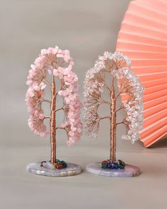 two pink and white trees on marble bases in front of an orange fan with beads