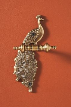 an ornate brass door handle with a peacock on it's side and a red wall in the background